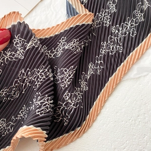 Close-up of pleated floral silk scarf with dark grey base and orange contrast border