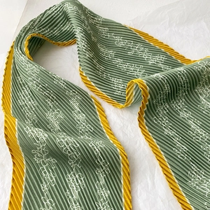 Detail of sage green pleated skinny scarf featuring white floral prints and yellow borders