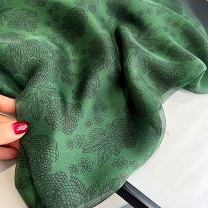 Detail of emerald green silk scarf with black floral print and delicate rolled edges