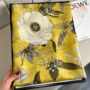 Detail of yellow floral silk scarf folded in a gift box with sunglasses and a magazine