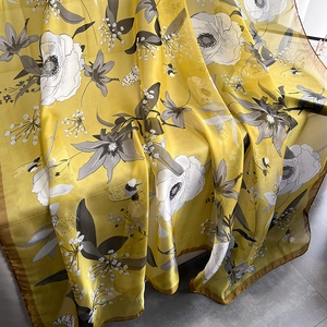 Bright yellow silk-like floral scarf with bee print displayed on a bench