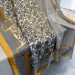 Detail of luxury houndstooth silk scarf with gold horsebit pattern on a gray sofa