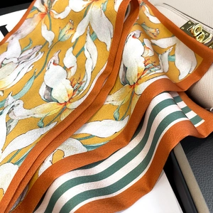 Détail d'un foulard en soie jaune à fleurs blanches et rayures vertes sur un sac blanc