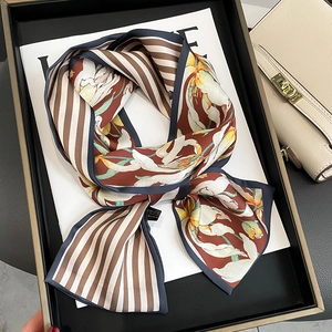 Foulard élégant en soie à fleurs et rayures noué sur l'anse d'un sac à main beige