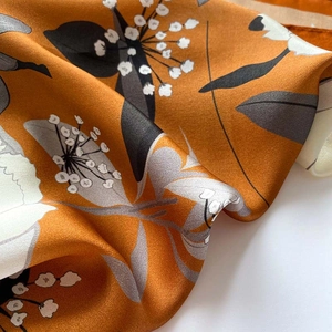 Detail of silk scarf showing orange fabric with white floral prints and soft texture