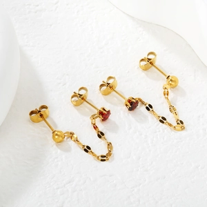Detail of gold chain earrings featuring red heart gems on a textured white base