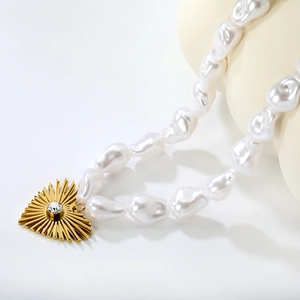 Collier de perles baroques avec pendentif cœur doré et pierre scintillante sur fond blanc
