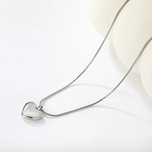 Detail shot of silver heart pendant on a thin snake chain necklace in a minimalist setting