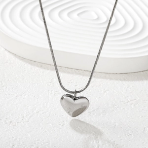 Close-up of polished silver heart pendant on a sleek snake chain with white texture