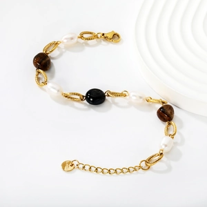 Bracelet en acier inoxydable doré avec œil de tigre et perles sur un support blanc ondulé