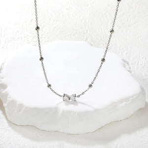 Primer plano del collar con colgante de lazo plateado y circonitas sobre piedra