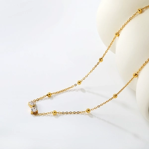 Detalle de collar de cadena de bolas doradas con dos colgantes de circonita en forma de corazón