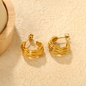Boucles d'oreilles créoles torsadées en C plaquées or 18 carats sur fond beige