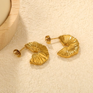 Macro detail of gold fan-shaped pleated stud earrings on a textured beige surface