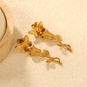 Vue macro de boucles d'oreilles en acier doré avec détails de papillon et fleur de rose