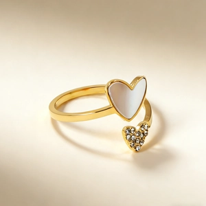 Dettaglio di un anello a cuore dorato con madreperla e zirconi su sfondo caldo