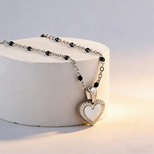 Silver stainless steel necklace with heart shell pendant and black beads on white stand