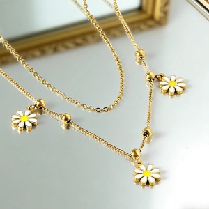 Gros plan d'un collier doré double rang avec pendentifs marguerites sur fond miroir