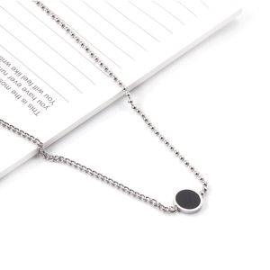 Collier chaîne asymétrique en acier inoxydable avec pendentif noir sur un carnet blanc