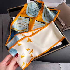 Elegant bird print skinny silk scarf with orange borders draped over a brown leather handbag
