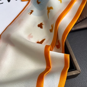 Detailed macro shot of a silk scarf with orange bird prints and fine satin texture