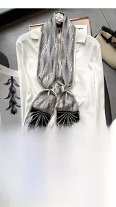 Gros plan d'un foulard étroit en soie à motifs géométriques noir et blanc sur un sac à main