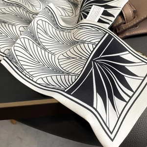 Détail d'un foulard en soie noir et blanc avec motifs géométriques sur un sac en cuir