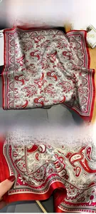 Macro detail of red paisley silk scarf showing fine edge stitching on wooden background
