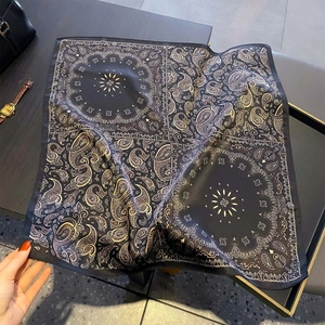 Detail of premium silk square scarf featuring gold paisley print on a black silk surface