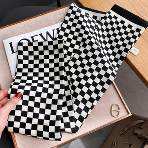 Écharpe étroite en soie à motif damier noir et blanc posée sur un sac et un magazine