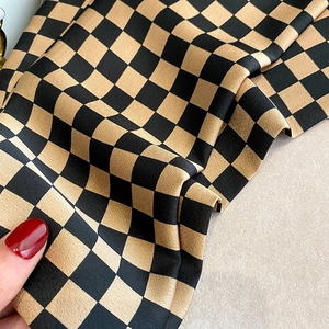 Gros plan sur l'écharpe en soie à damier noir et or avec une finition satinée élégante