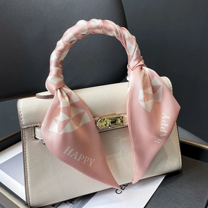 Pink geometric pattern silk scarf with HAPPY lettering tied on a leather bag handle