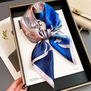 Elegant silk scarf with orange and blue floral print tied in a bow on a white book