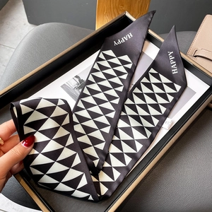 Detail of a geometric black and white silk twilly scarf with HAPPY lettering on a display box