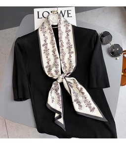 Détail d'un foulard en soie à fleurs porté avec un haut en tricot noir et accessoires