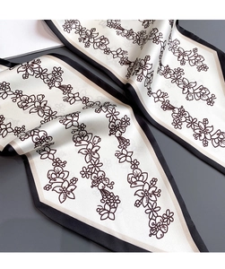 Détail d'un foulard étroit en soie à motif floral montrant la texture satinée et les bords