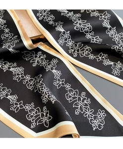 Détail du motif floral et bordure dorée sur écharpe étroite en soie noire de qualité