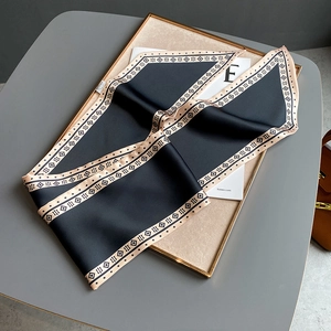 Nahaufnahme von schwarzem Seidenschal mit beigem Geometrie-Muster auf einem Tablett