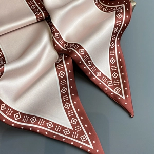 Detail eines champagnerfarbenen Satinschals mit geometrischem Muster und braunem Rand