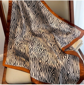 Detail of zebra print silk scarf with brown borders draped on a beige leather chair