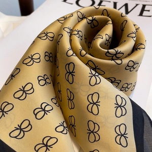 Detail of silky gold scarf with black butterfly print featuring elegant satin texture