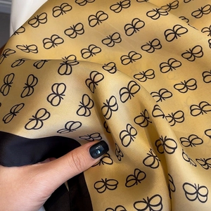 Detailed macro view showing the smooth silk texture and golden butterfly pattern on the scarf