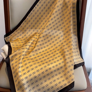 Detail of silk square scarf with yellow bow patterns draped on a wooden chair