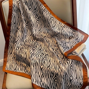Elegant zebra print silk square scarf with coffee brown borders draped on a chair