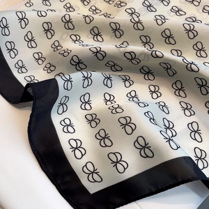 Detail of silk scarf showing black bow pattern and smooth texture on beige fabric