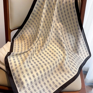 Detail of silk-feel square scarf with monogram print and black borders draped on chair