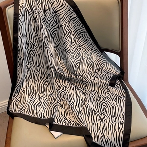 Detail of zebra pattern silk scarf with black satin border draped on a leather chair
