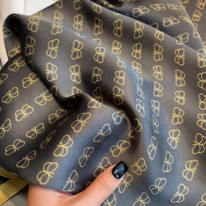 Detailed view of dark grey silk scarf with elegant golden butterfly print patterns