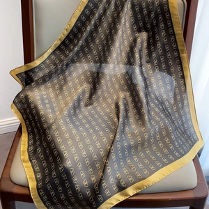 Detailed view of black silk scarf with gold butterfly pattern and satin gold borders