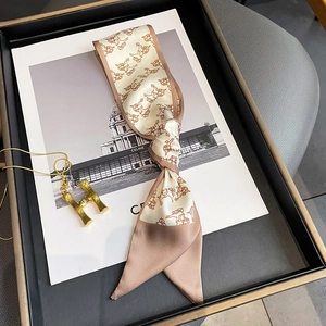 Detail of champagne satin silk scarf with horse print and gold H-pendant necklace
